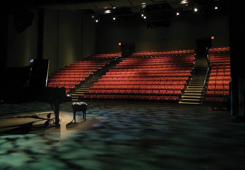 View of piano and audience seating from the back of the auditorium stage.