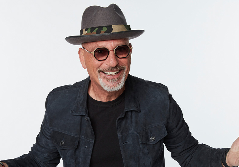 Howie Mandel smiling with his arms outstretched.